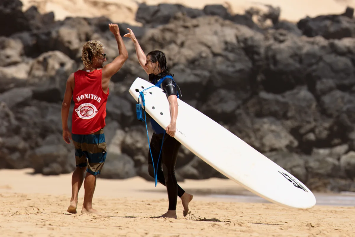 Surf instructor and student high-fiving on the beach in Corralejo, Fuerteventura